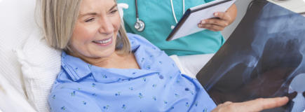 A patient is sitting in a hospital bed and smiling. Her doctor is showing her an x-ray of her successful hip replacement.